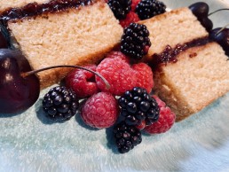 A slice of vanilla sponge cake with strawberry jam and fresh summer berries