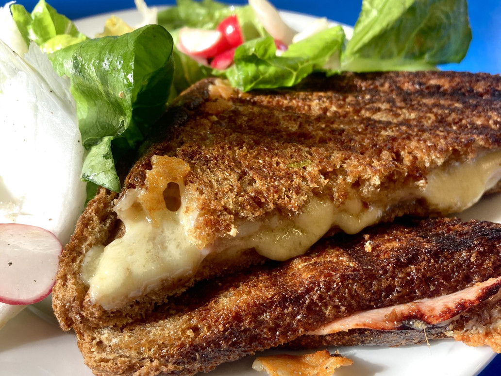 A toasted sandwich oozes melty cheese, on a plate with green salad