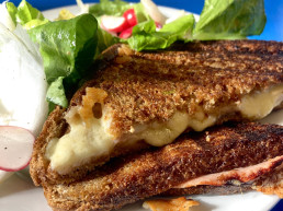 A toasted sandwich oozes melty cheese, on a plate with green salad