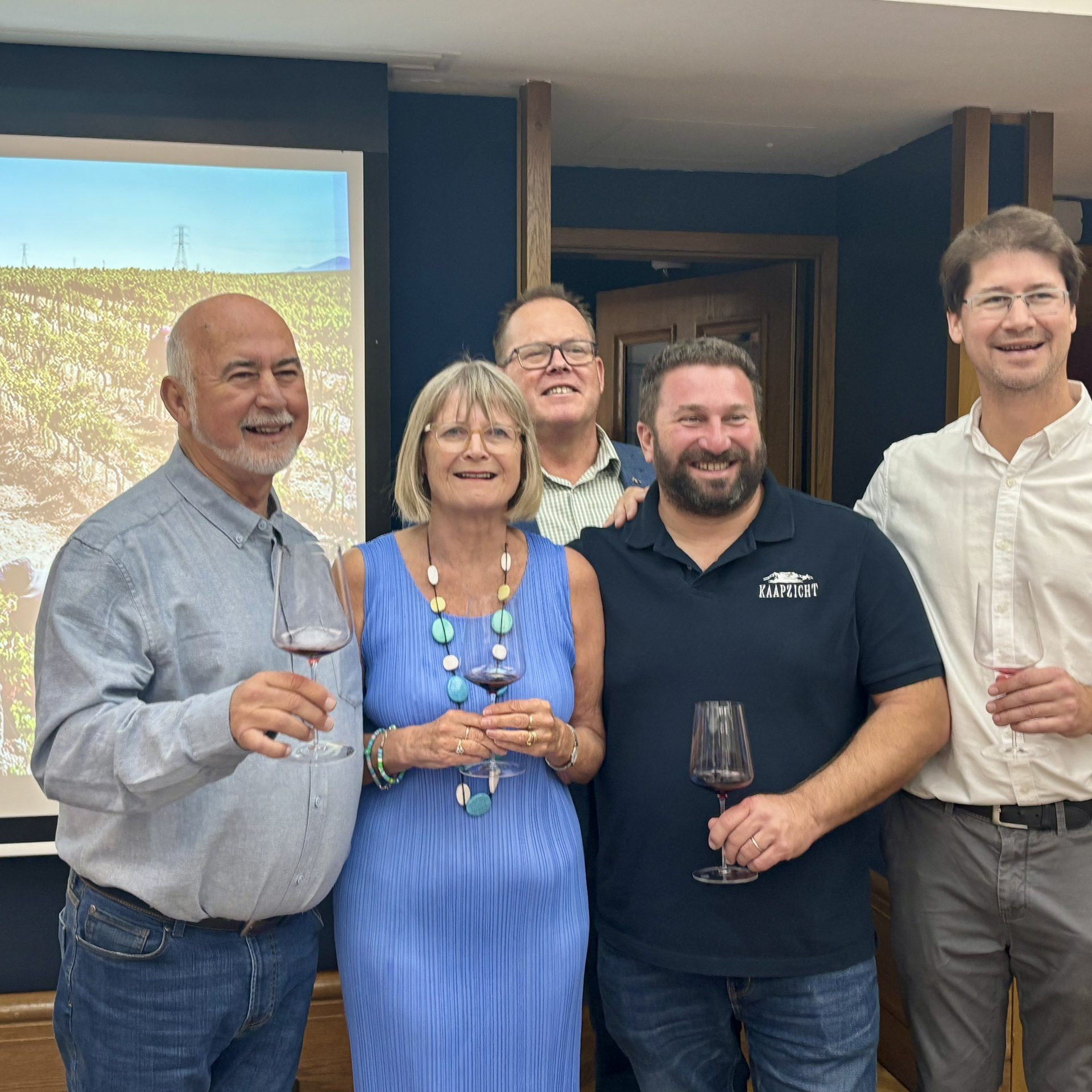 Four men and a woman stand in front of a projecion of a South African Pinotage vineyard